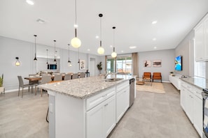 Een moderne keuken met witte kasten, granieten werkbladen en hangende lampen.
