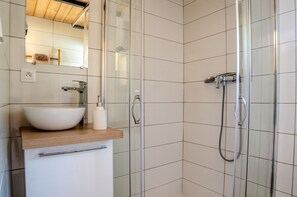 Et moderne badeværelse med hvid vask, spejl og bruser.