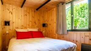Ein Zimmer mit Holzwandverkleidung, einem Bett, zwei Wandleuchten und einem Fenster mit Blick auf Grünflächen.