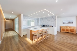A modern kitchen with a marble backsplash, wooden flooring, and a central island with bar stools.