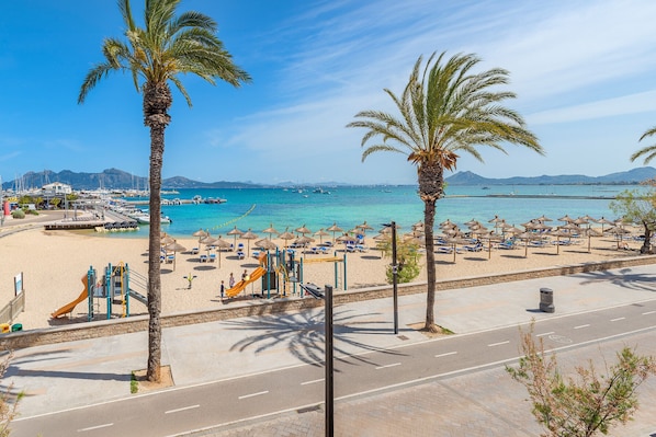 A beach with palm trees, a playground, and a clear blue sea.