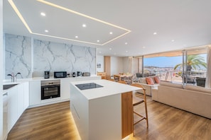 A modern kitchen with a marble backsplash, wooden flooring, and a dining area with a view.