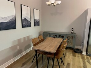 Un comedor con una mesa de madera y seis sillas, un aparador con detalles decorativos y tres cuadros en la pared.