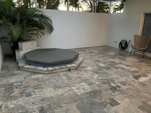 Un patio con suelo de piedra, un jacuzzi, una silla y una planta en maceta.