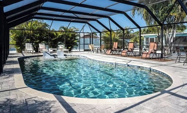 Relax by the pool surrounded by lush tropical plants and lounge chairs on a shaded deck.