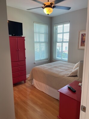 A bedroom with a bed, a red dresser, a ceiling fan, and a TV on a red cabinet.