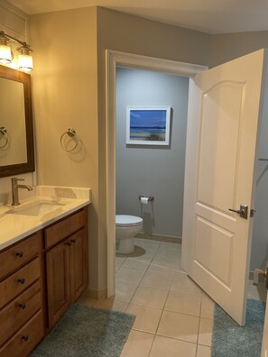 A bathroom with a sink, mirror, toilet, and a framed picture on the wall.
