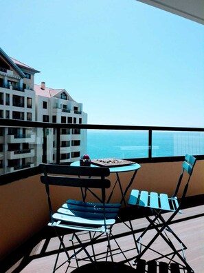 A balcony with two chairs and a small table, overlooking a building and the sea. - 2 Towers Sea View in Funchal Swimming Pool & Tennis (Funchal)