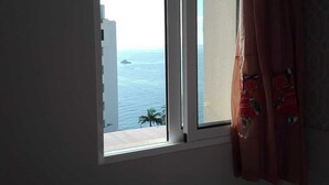 Quarto com janela para uma praia e oceano.