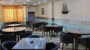 Un restaurante con mesas y sillas redondas, un adorno de barco en la pared y un suelo con estampado de cuadros.