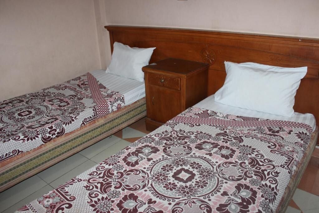 Two single beds with patterned bedding, a wooden nightstand, and a tiled floor.