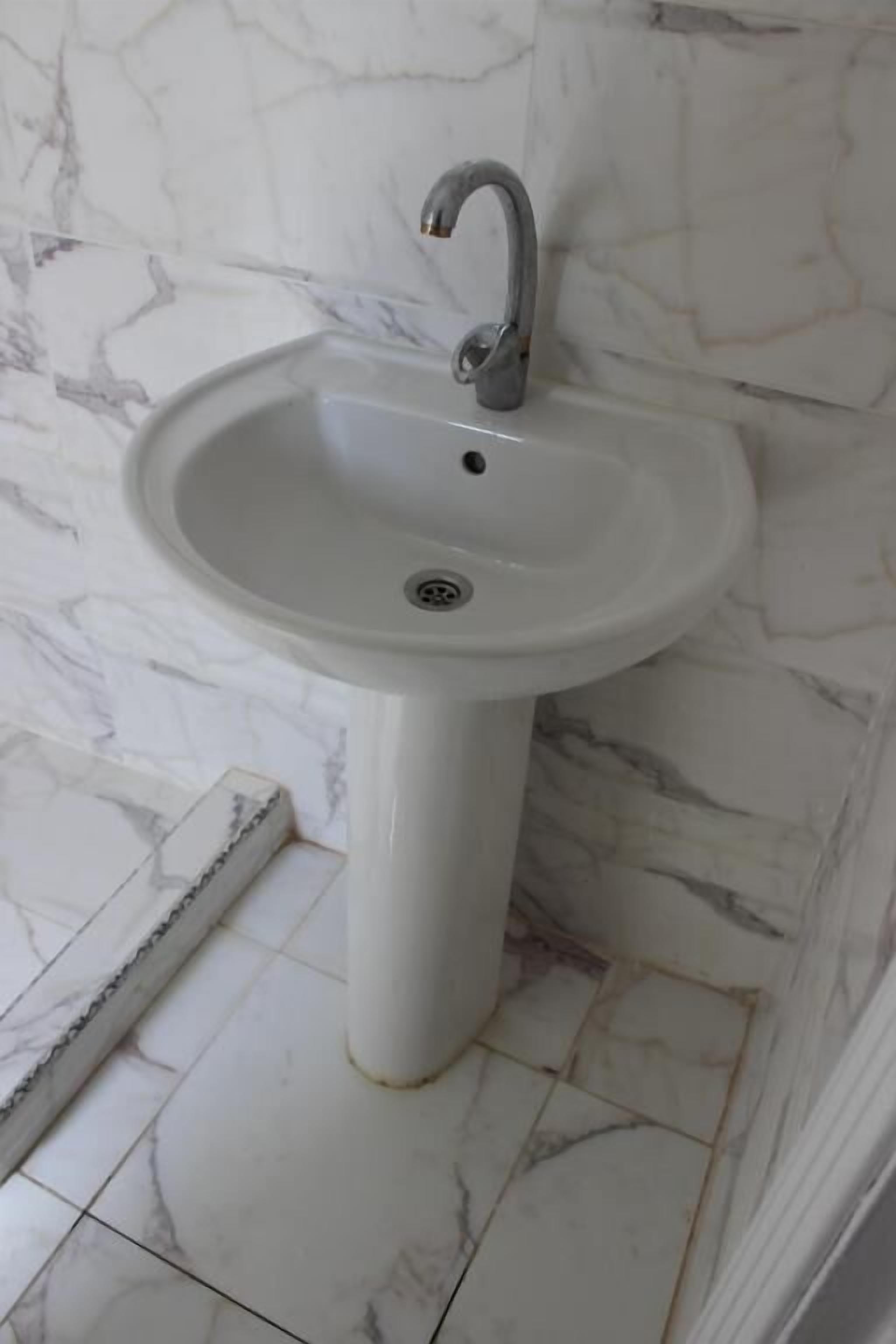 A bathroom with a white pedestal sink, marble walls, and white tiled flooring.