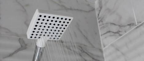 A showerhead with water running in a bathroom with marble tiles.