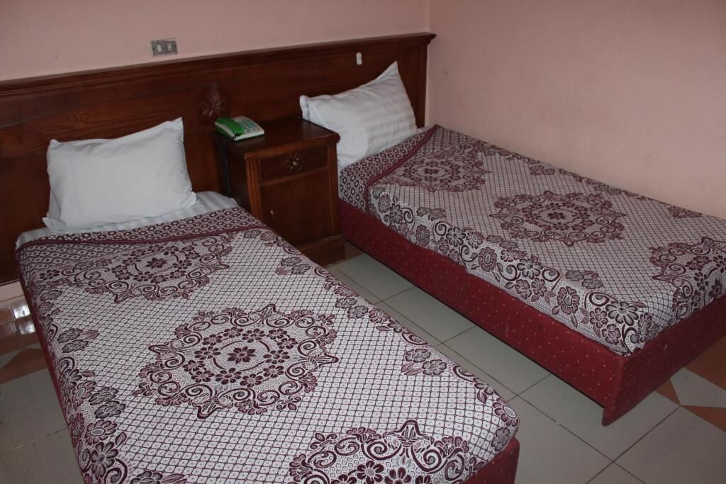 Two single beds with patterned bedding, wooden headboards, and a nightstand with a green object.
