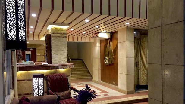 Un vestíbulo con mostrador de recepción, una escalera y una zona de estar con un jarrón decorativo.