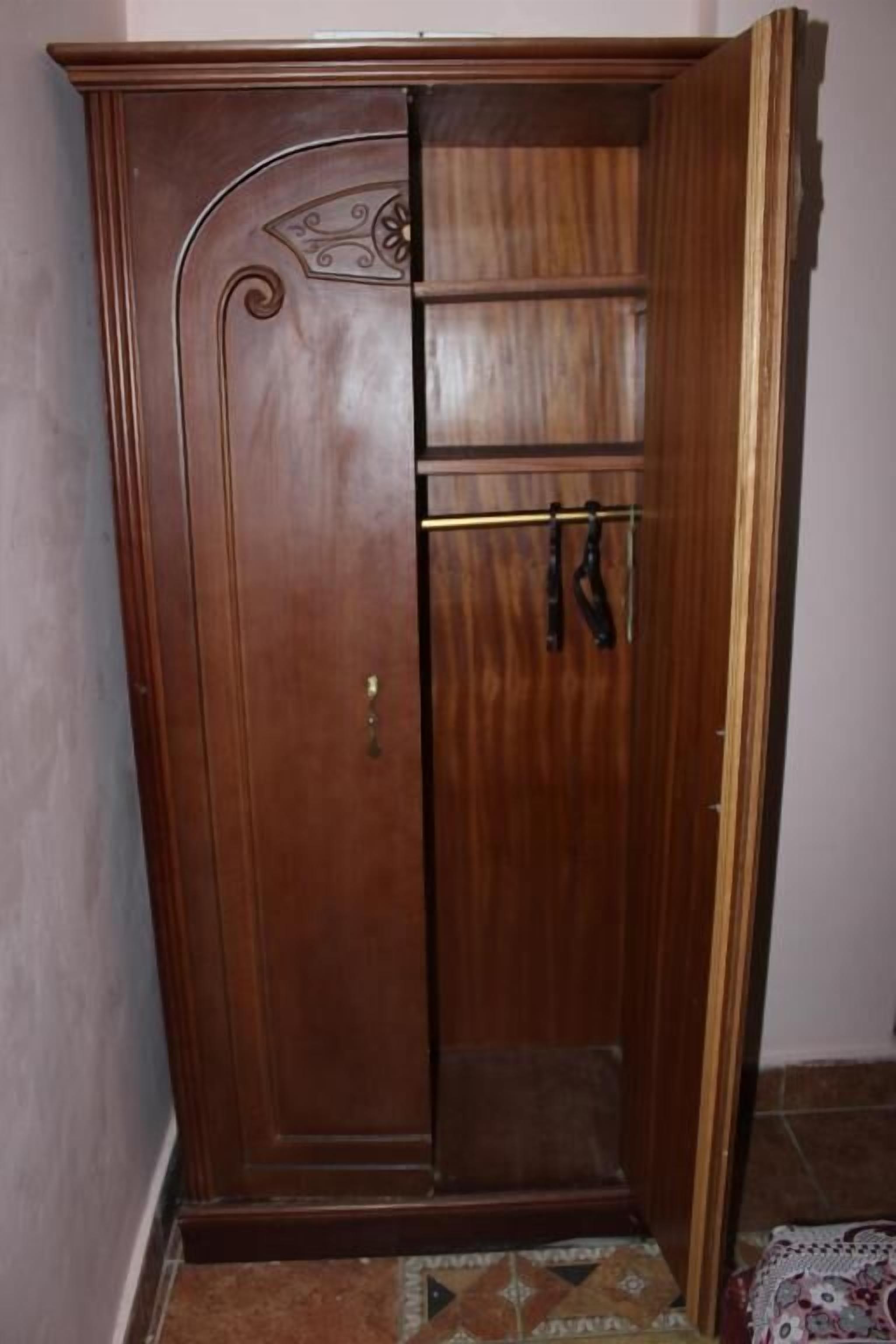 Un armario de madera con puerta de espejo, un estante pequeño y una barra para colgar.