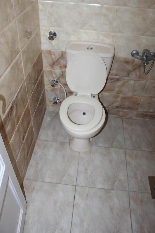 A bathroom with a toilet, a shower, and a tiled floor. - Sea Star Hotel (Alexandria)