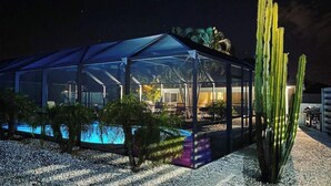 Une structure de type serre, dotée d’un toit transparent, d’une piscine et d’un cactus au premier plan.