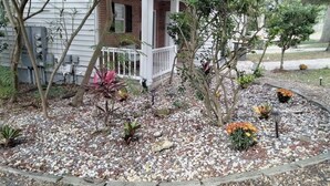 Ein Haus mit Veranda, Backsteinelementen und einem Garten mit verschiedenen Pflanzen und Kieselsteinen.