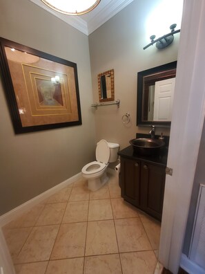 Une salle de bain équipée de toilettes, d’un lavabo, d’un miroir et d’une œuvre d’art encadrée accrochée au mur.