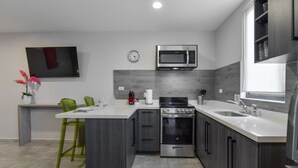 A modern kitchen with a central island, stainless steel appliances, and a flat-screen TV mounted on the wall.