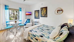 Hotellihuone, jossa on sänky, työpöytä, tuoli, televisio ja kattotuuletin.