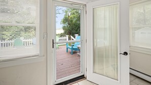A view from inside a room with a sliding glass door leading to an outdoor deck with a wooden floor and a blue chair. - Causeway Cottage: Lake Beach & NY Biking Ferry (Colchester)