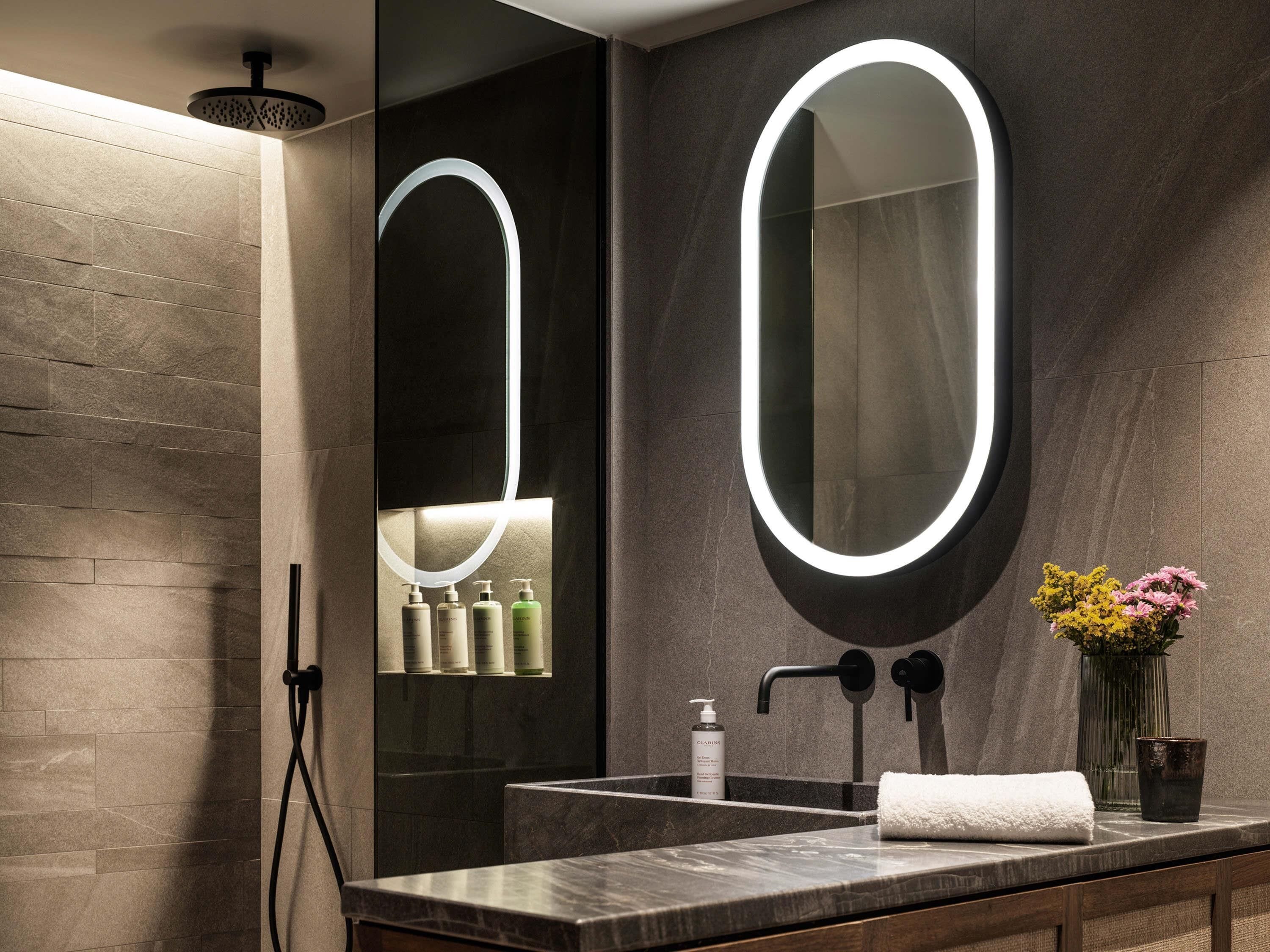 A modern bathroom with a large mirror, a showerhead, a sink, and toiletries.