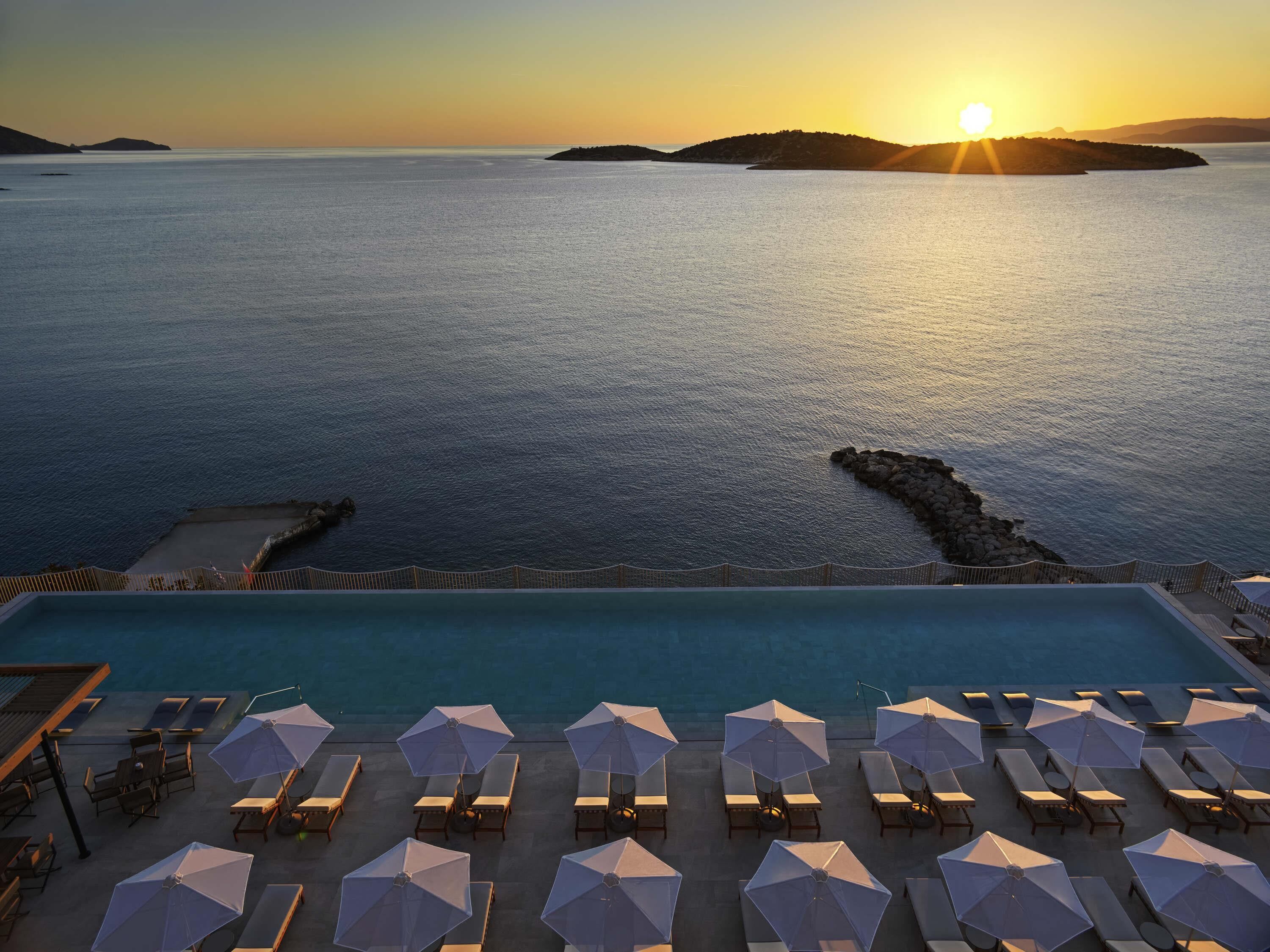 A pool with sun loungers and umbrellas, overlooking a calm sea with distant islands.