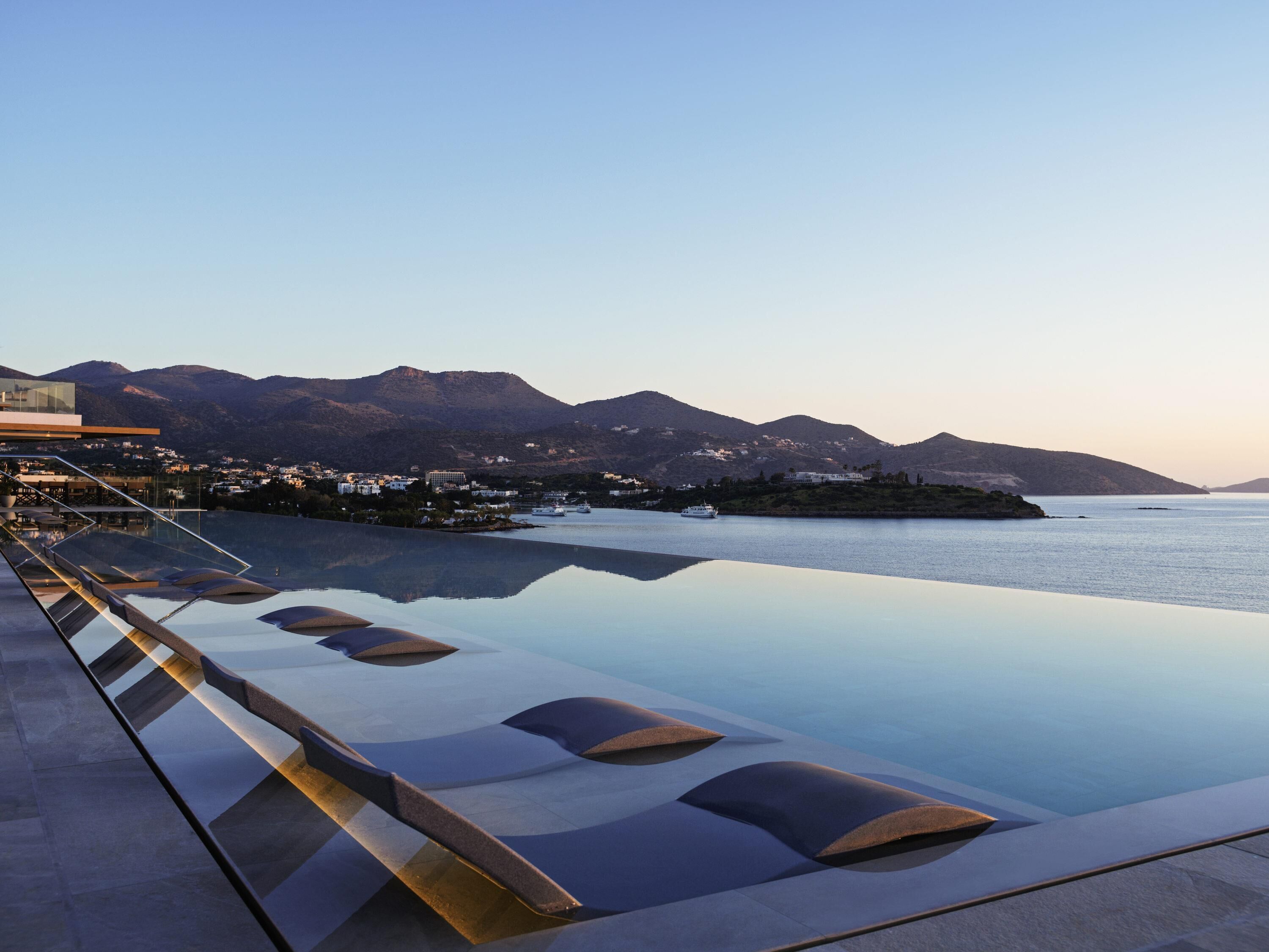 A infinity pool with a clear view of a mountainous coastline and a distant cityscape.