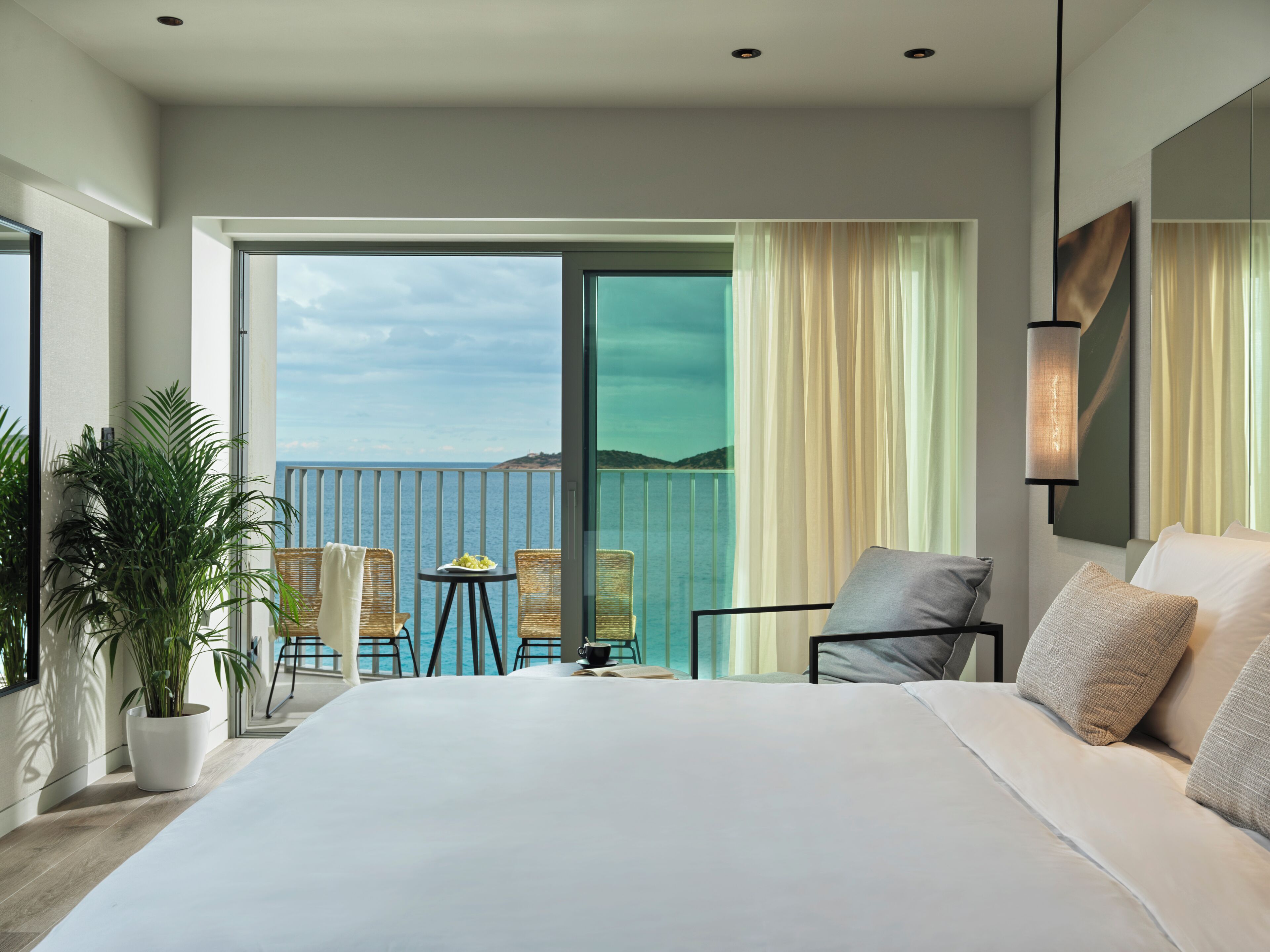 Une chambre d’hôtel moderne dotée d’un grand lit, d’un balcon avec vue sur la mer et d’un coin repas avec une table et des chaises.