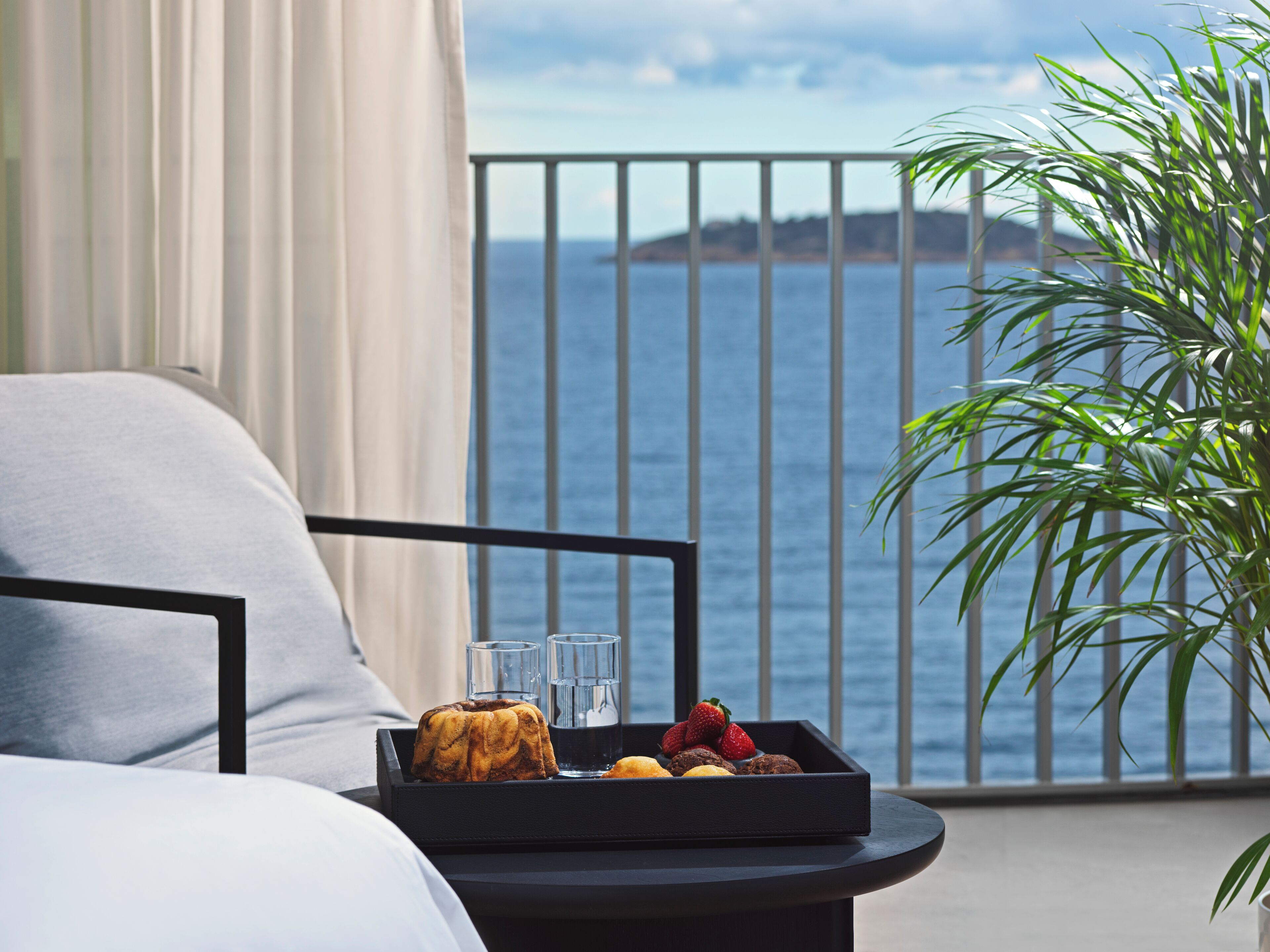 Un balcón con una bandeja de comida, una planta y vista al mar.
