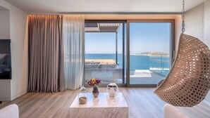 A modern room with a large sliding glass door leading to a balcony with a view of the sea. There is a hanging chair, a table with a vase of flowers, and a decorative item on the table.
