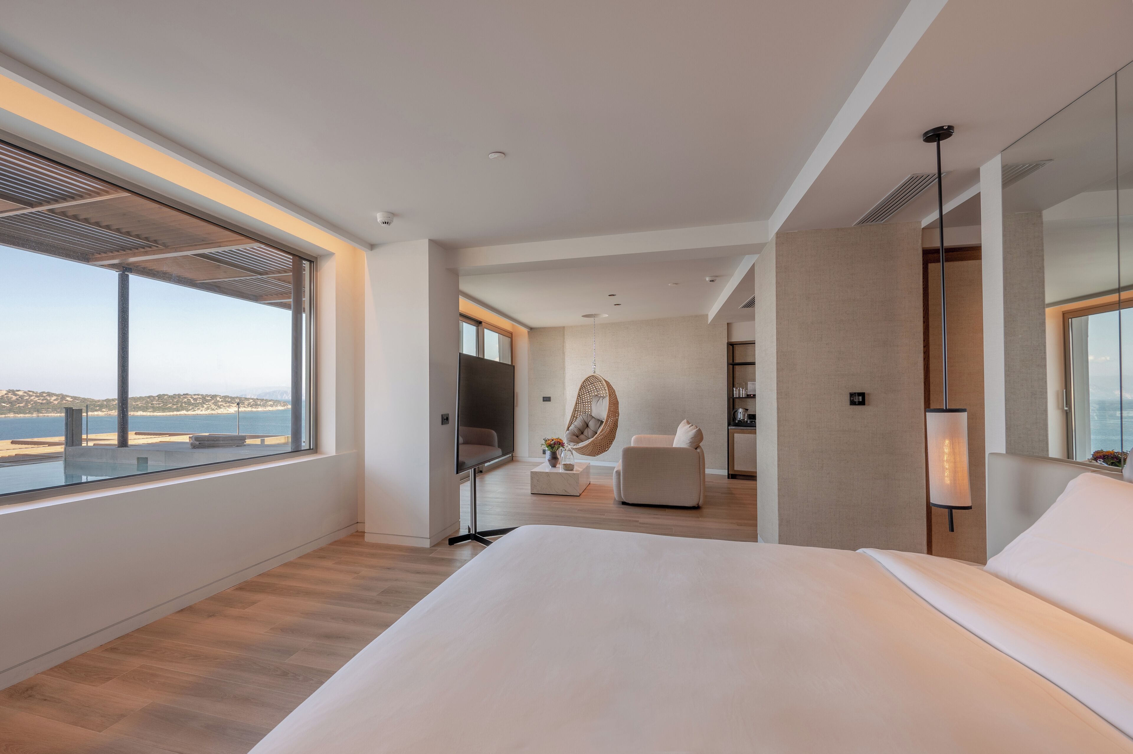 Une chambre d’hôtel moderne dotée d’un grand lit, d’un coin salon avec un fauteuil suspendu, d’une télévision et offrant une vue sur la plage.