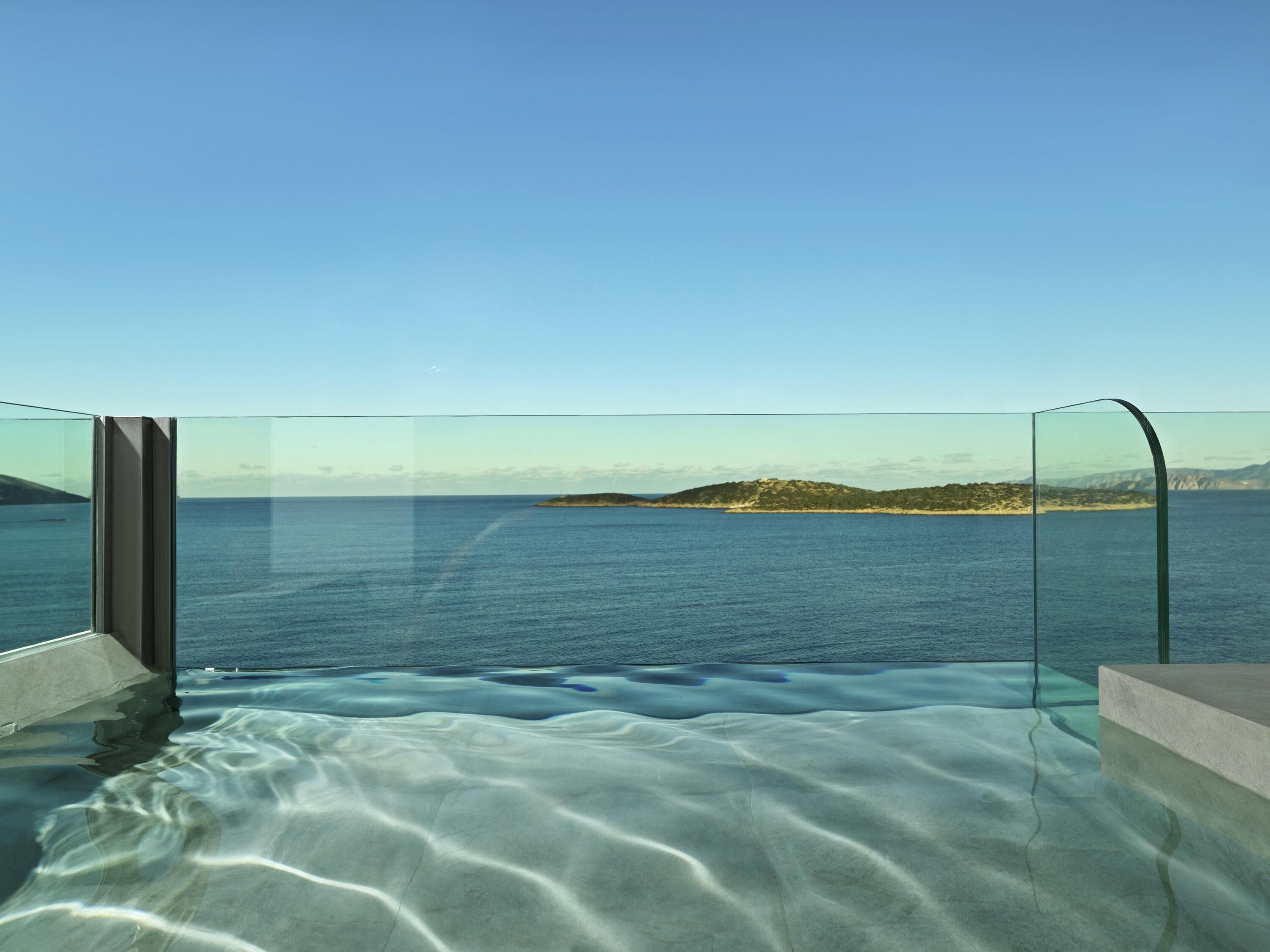 En pool med oändlig horisont, omgiven av glasväggar, med fri utsikt över havet och det avlägsna landskapet.