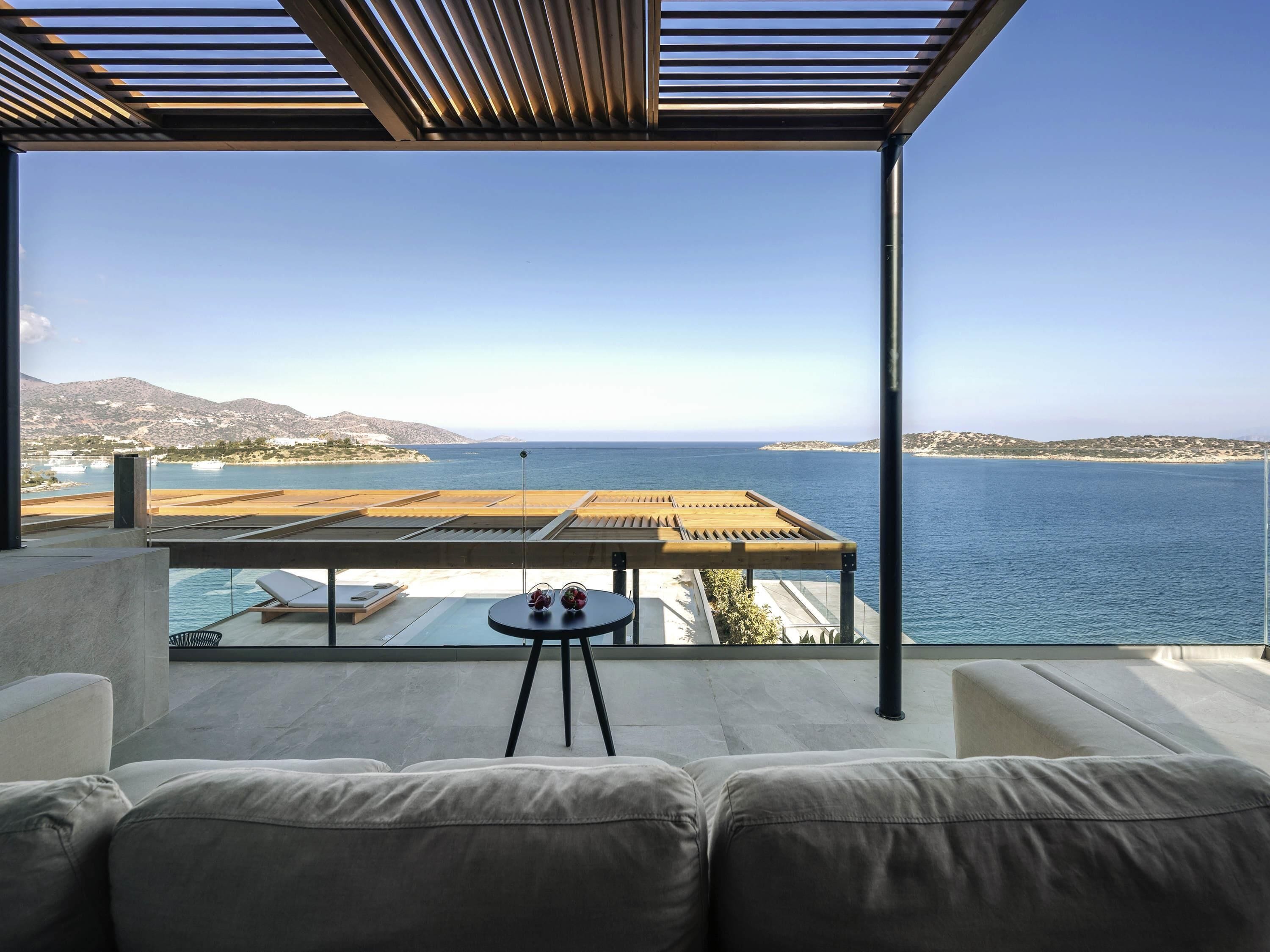 A balcony with a view of the sea, a pool, and a table with flowers.