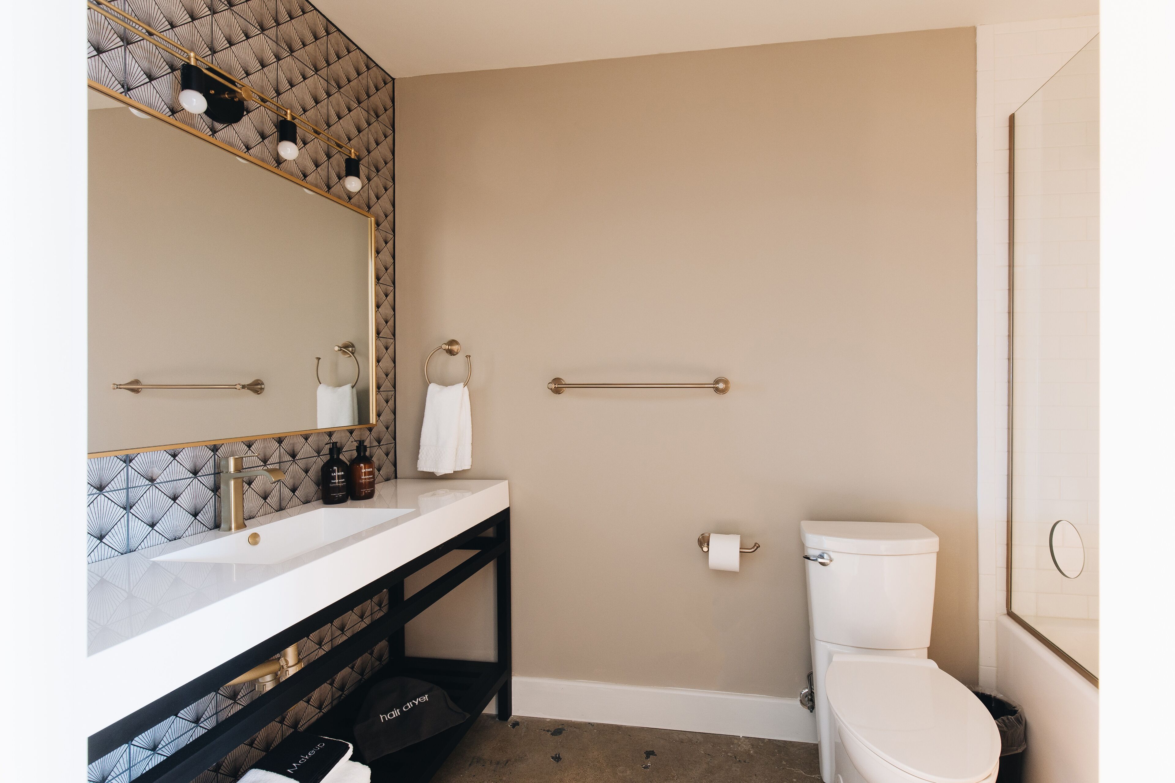 Een badkamer met een witte wasbak, spiegel en toilet. Daarboven hangt een handdoekhouder en er is een handgreep naast het toilet.