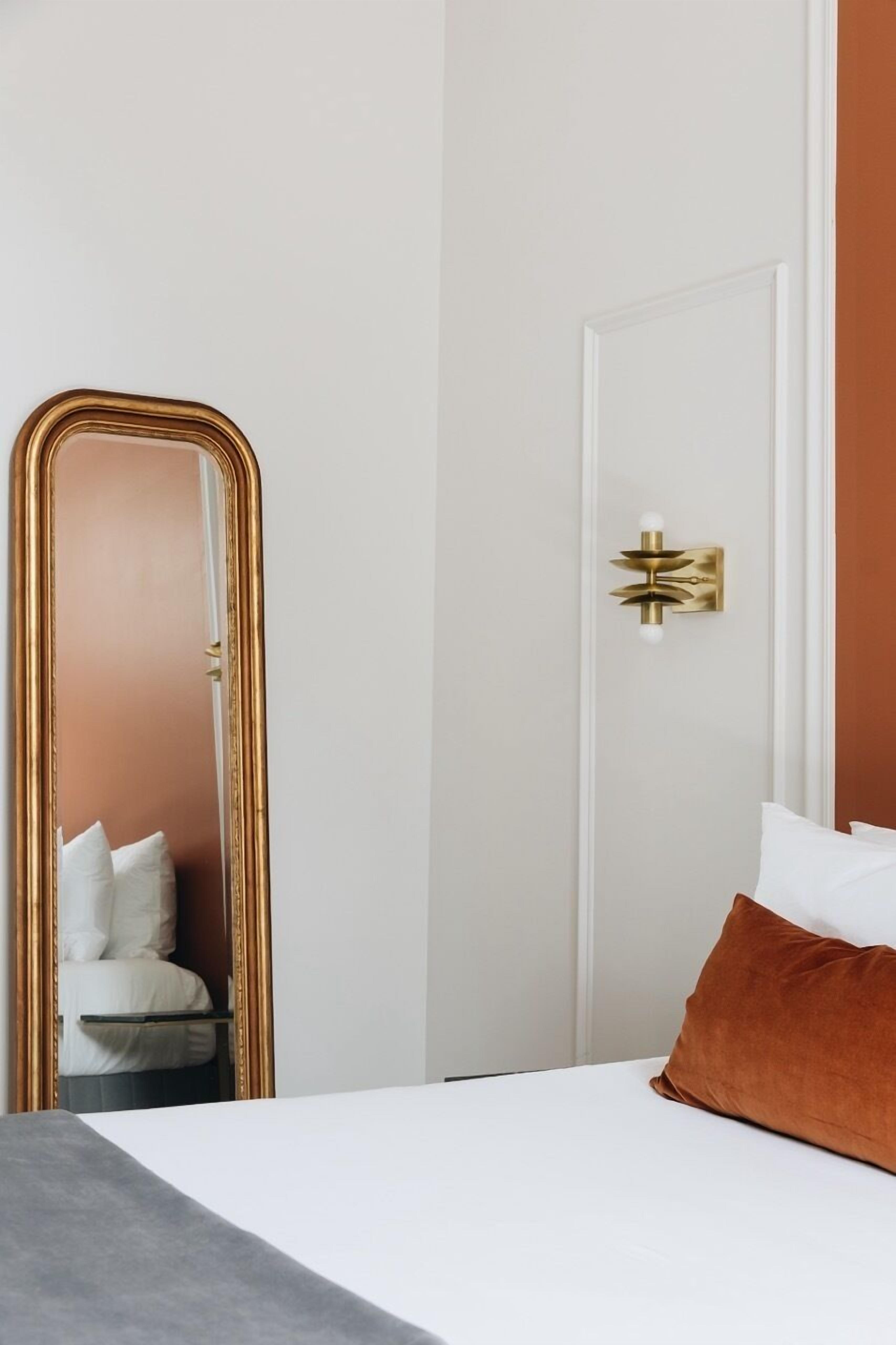 A bedroom with a bed, a large mirror, a door with a light fixture, and a brown pillow.