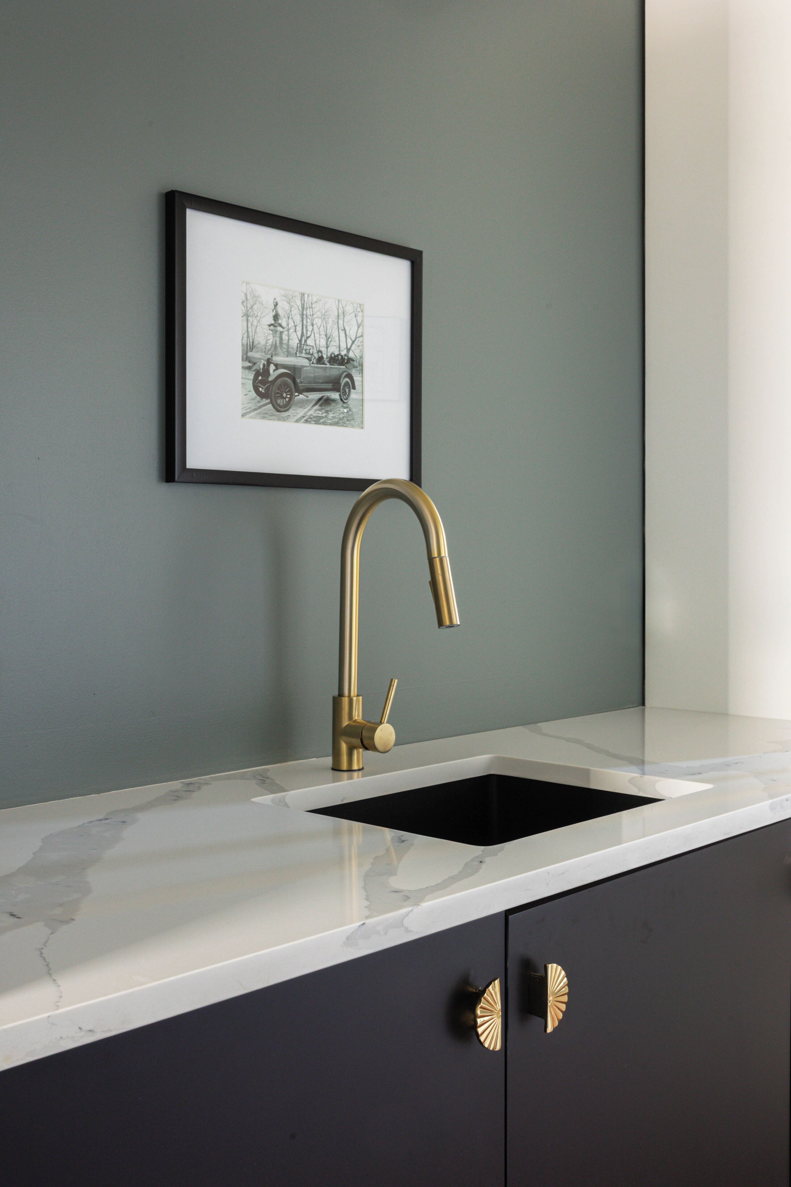 A kitchen with a marble countertop, a gold faucet, and a framed picture on the wall.