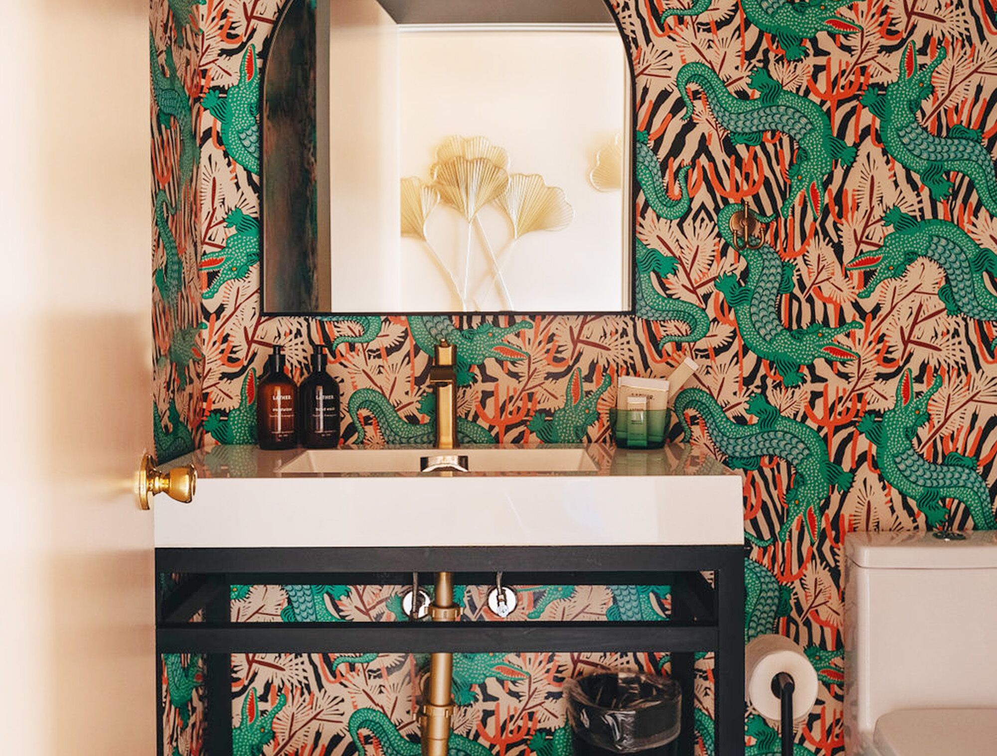 Een badkamer met een wastafel, spiegel en toilet. De muren zijn versierd met een patroon van groene en oranje bladeren.