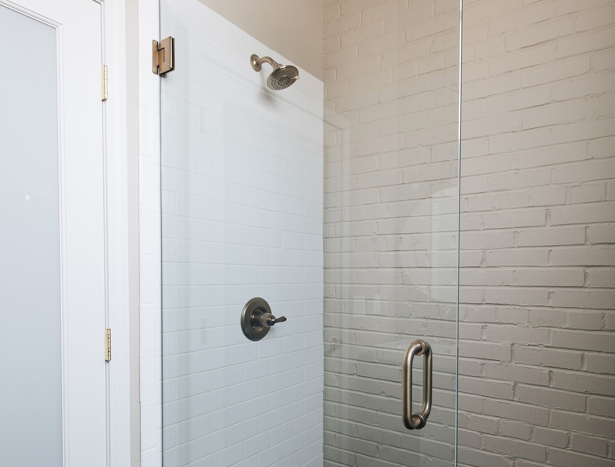 Une douche avec une porte en verre, des murs recouverts de carreaux blancs et un motif en briques.