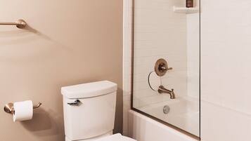 A bathroom with a toilet, a glass shower enclosure, and a white tiled wall.