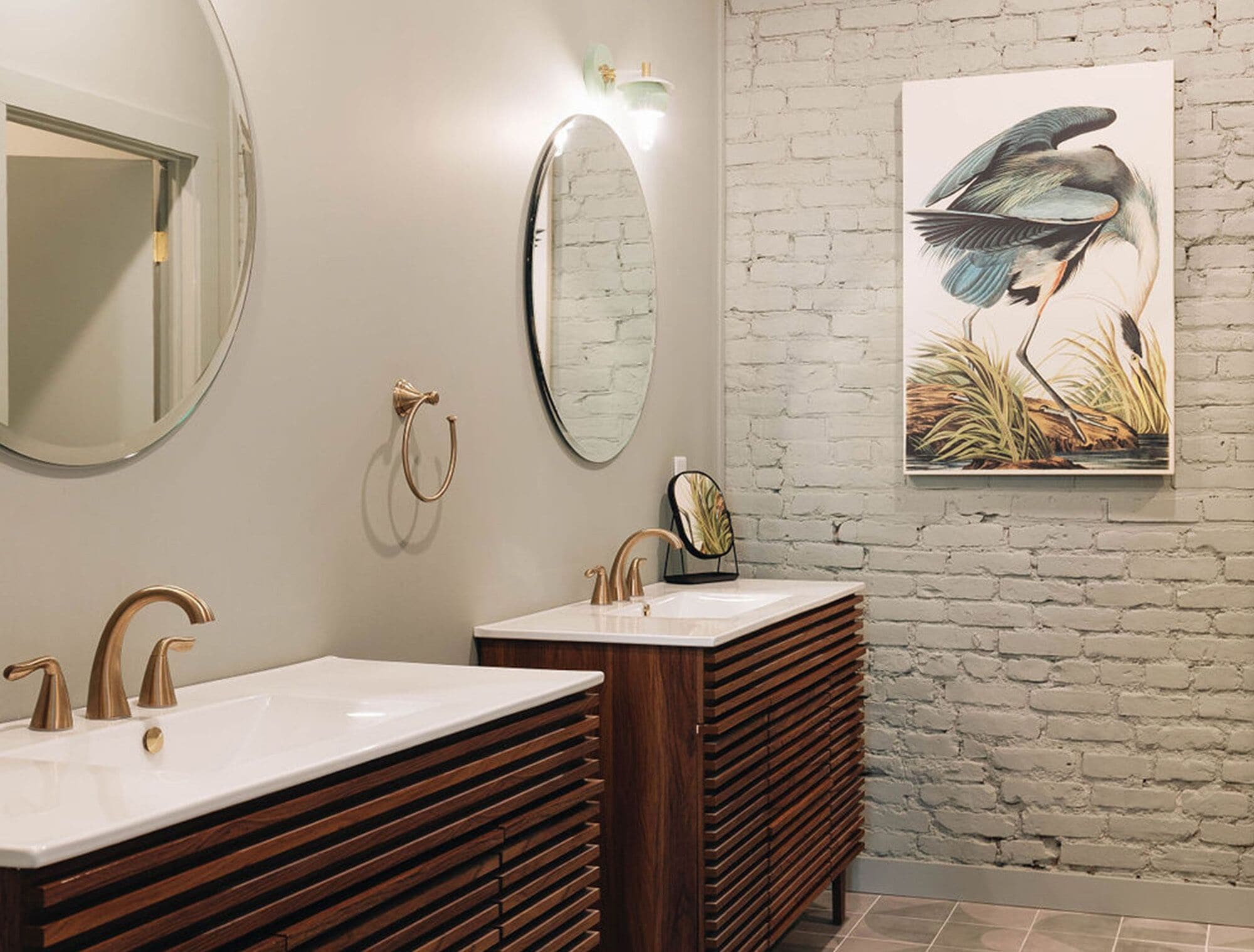 A bathroom with two sinks, a round mirror, and a wall-mounted light fixture.