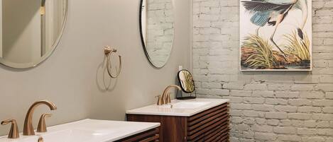 A bathroom with two sinks, a round mirror, and a wall-mounted light fixture.