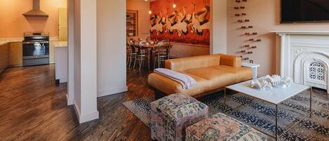 A modern living room with a sofa, ottomans, a fireplace, and a dining area with a large painting.