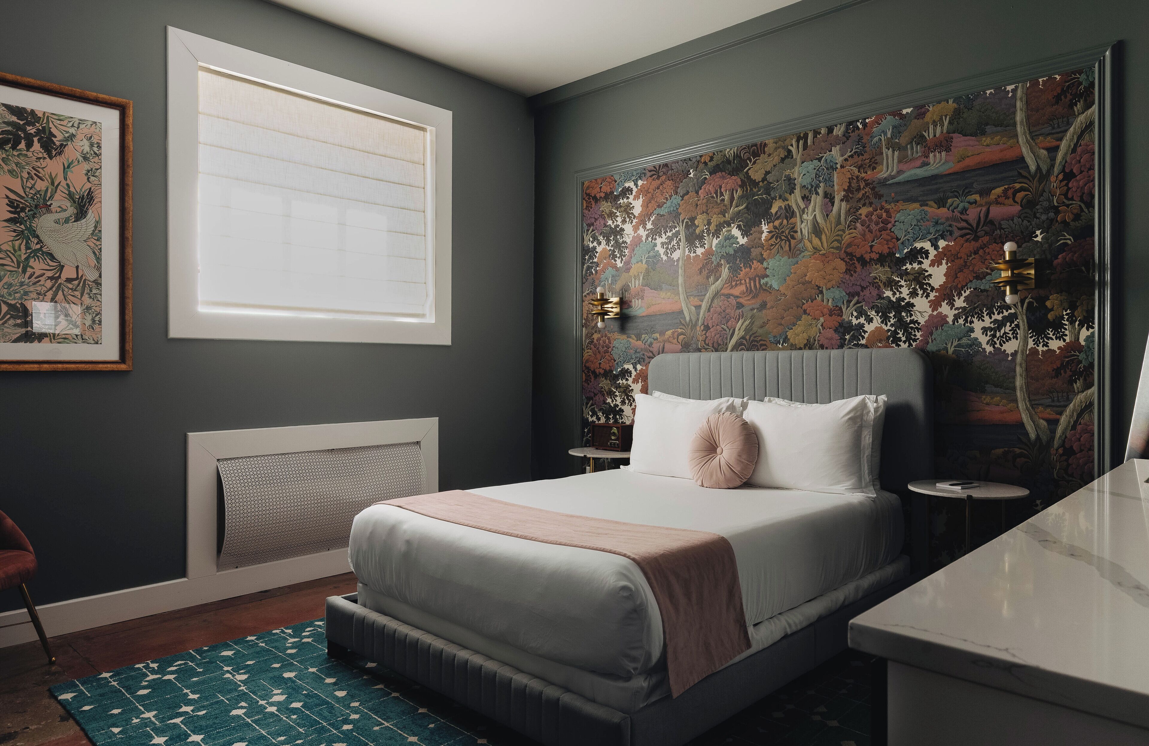 Une chambre à coucher avec un grand lit, une fenêtre, un radiateur, une table de chevet et un tableau accroché au mur.