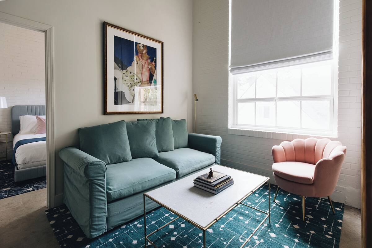 A room with a teal sofa, a white coffee table, a pink armchair, and a framed picture on the wall.