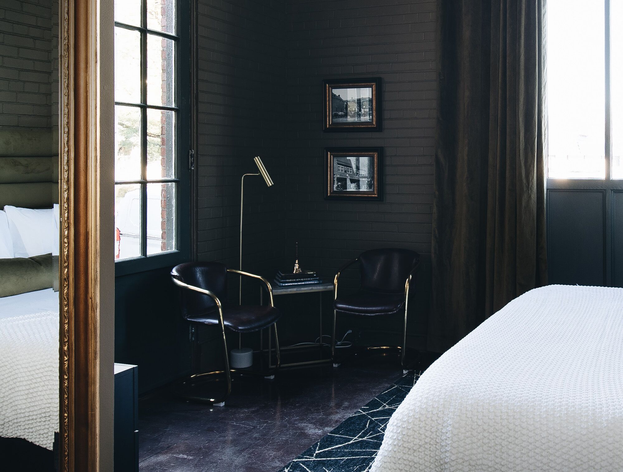 A hotel room with a bed, two chairs, a small table, and two framed pictures on the wall.