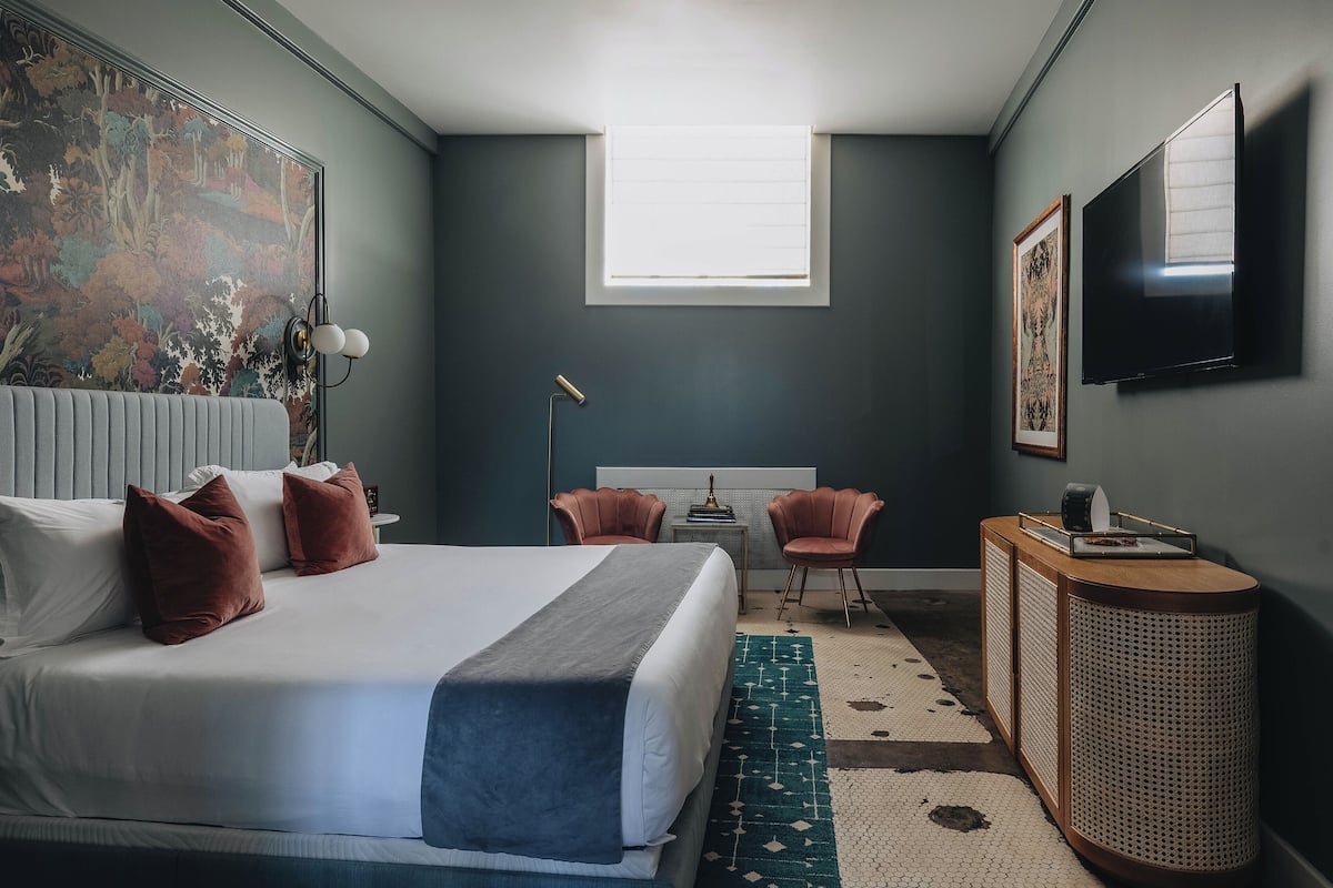 A bedroom with a bed, a desk, a chair, a television, and a window.