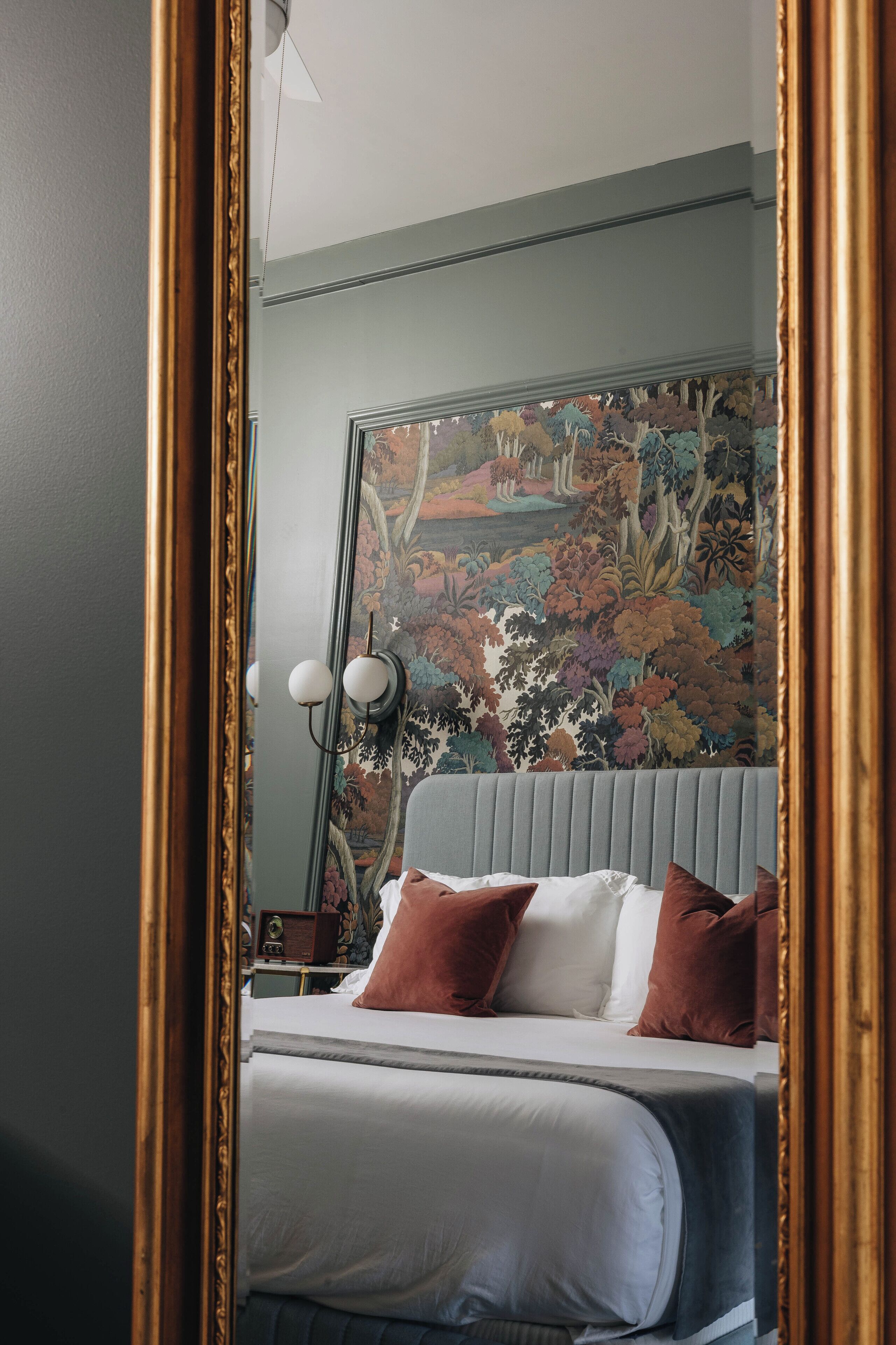 Un dormitorio con una cama, una mesita de noche, una lámpara y una pared decorada con un mural floral.
